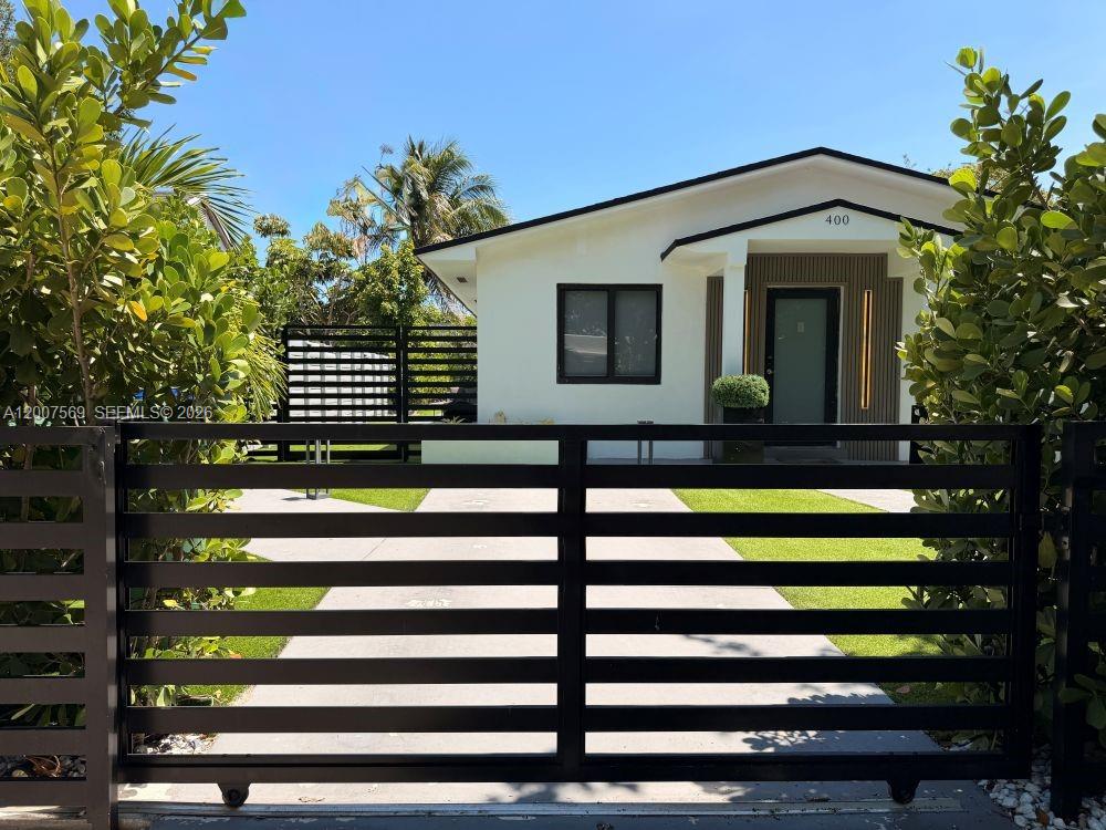 A white house with a black gate and a paved driveway sits behind lush greenery — 400 NW 40th St, Miami FL 33127, MIAMI, FL