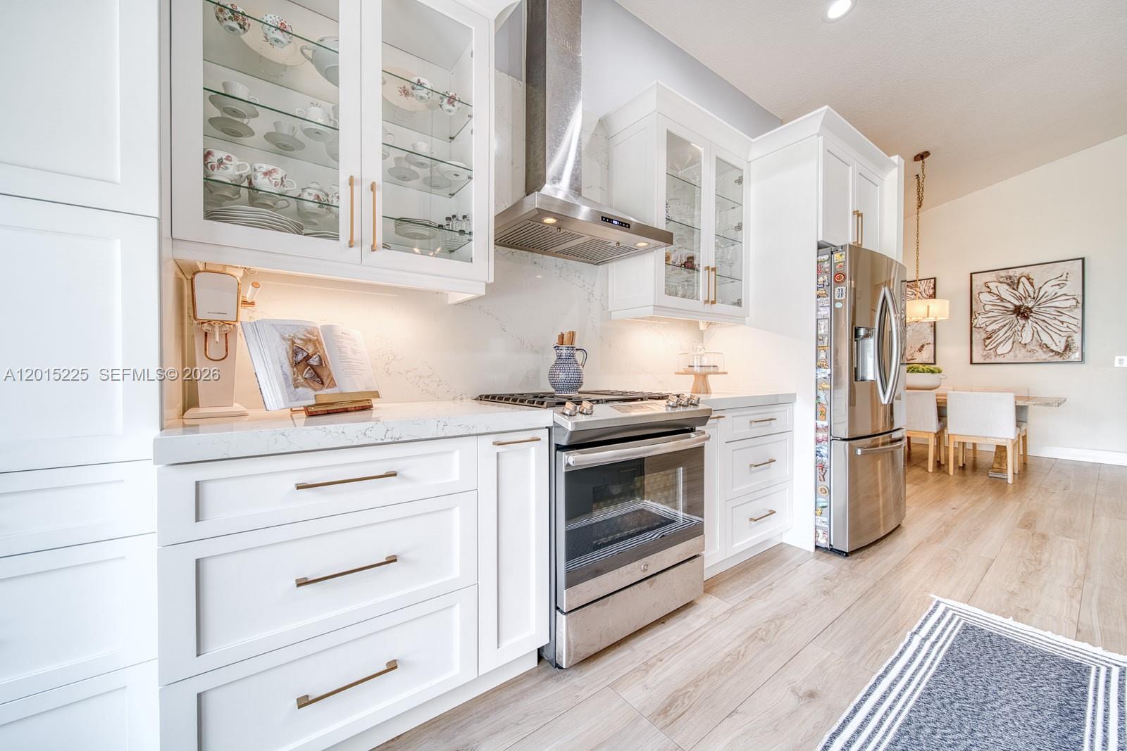 A modern kitchen features white cabinetry, stainless steel appliances, and light wood-look flooring — 77 Gables Blvd, Weston FL 33326, WESTON, FL