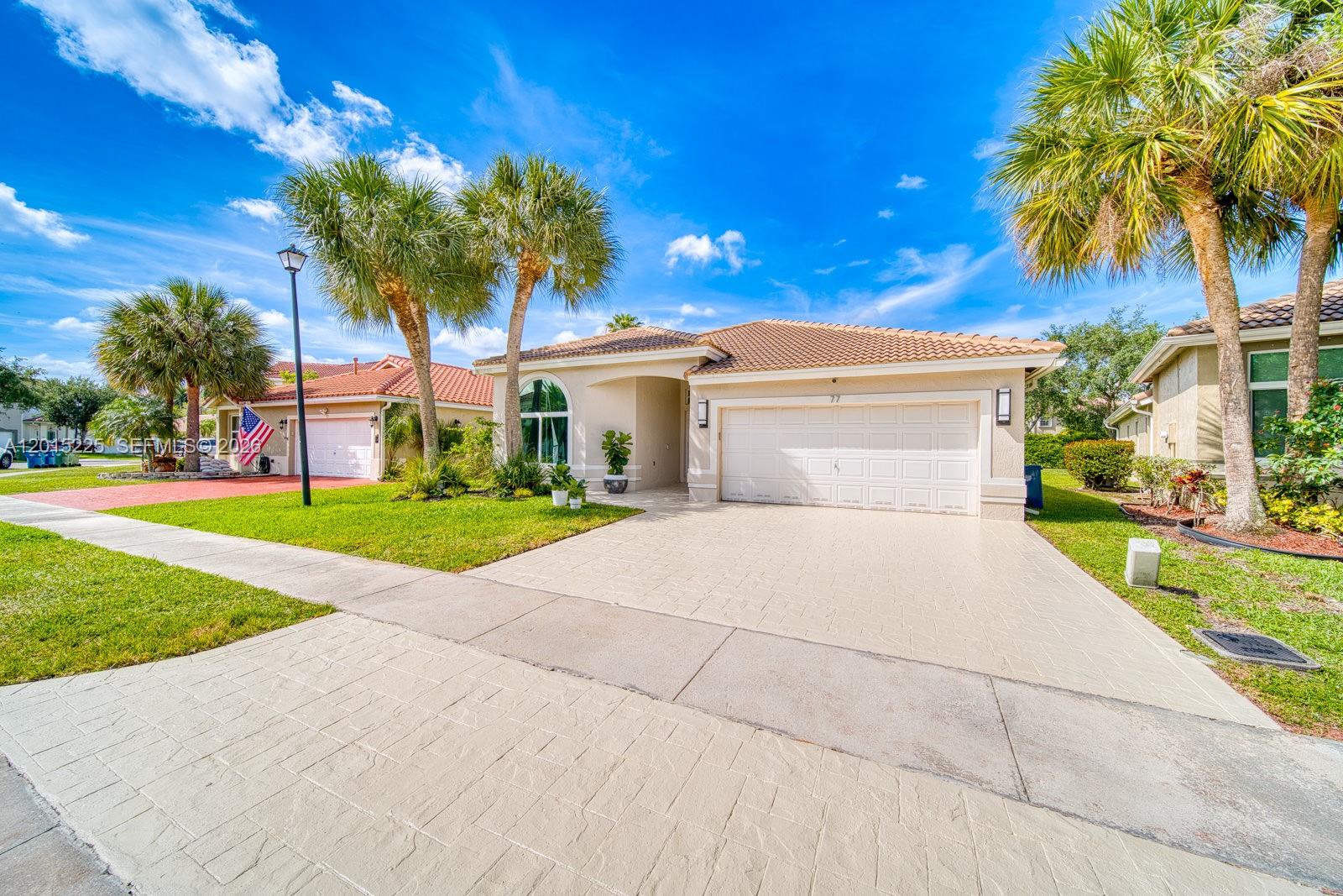 A single-story suburban house with a beige stucco exterior, tile roof, and paved driveway — 77 Gables Blvd, Weston FL 33326, WESTON, FL