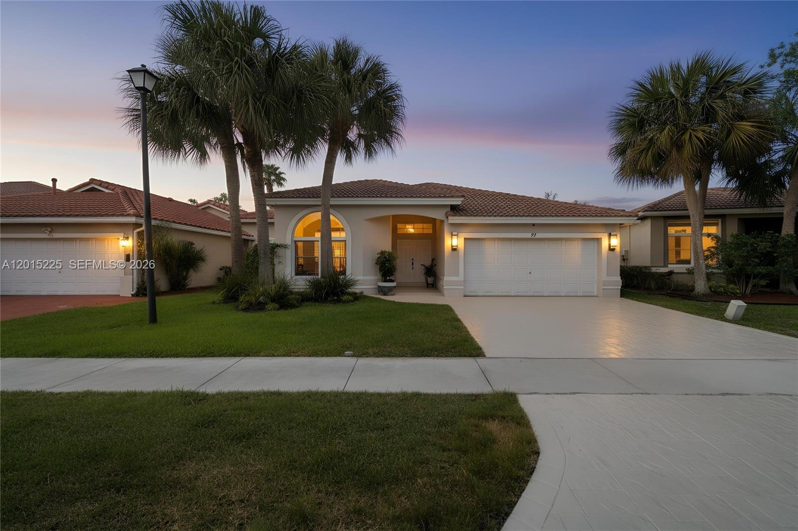 A single-story house with a tiled roof, white garage door, and palm trees at dusk — 77 Gables Blvd, Weston FL 33326, WESTON, FL