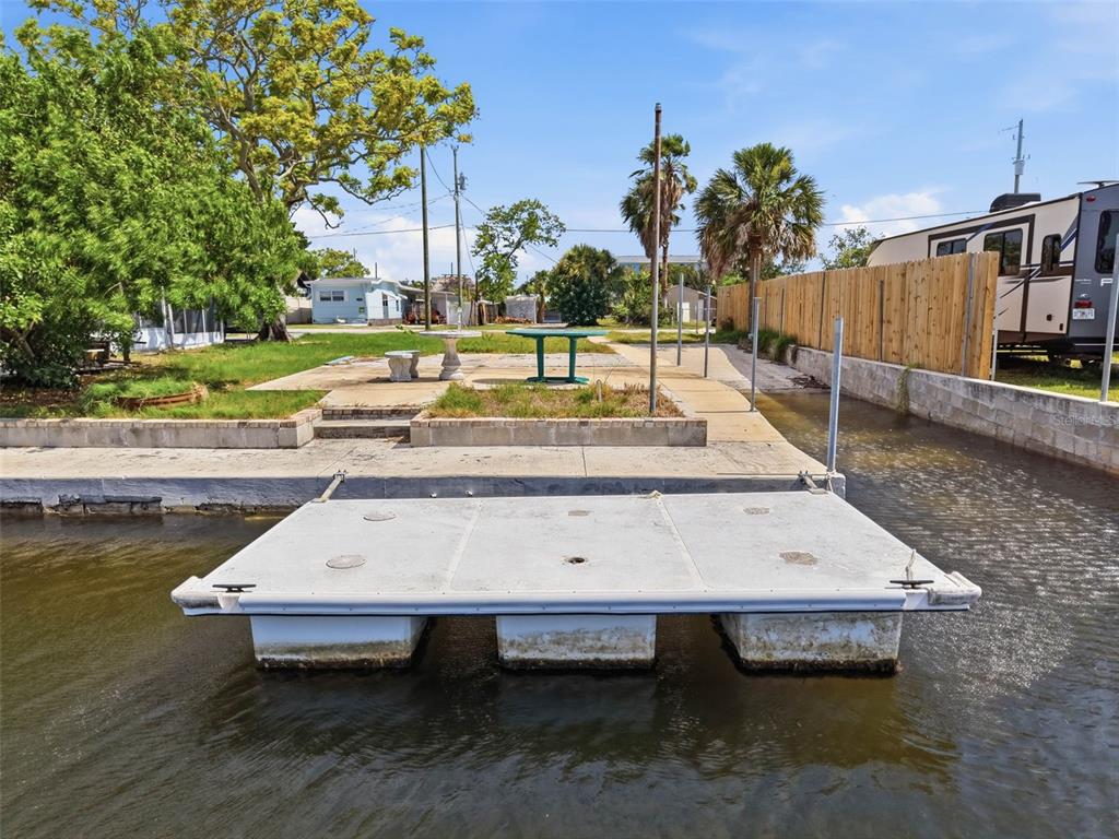 A floating dock sits in a canal in front of a yard with a table — 6737 OSPREY LANE, HUDSON, FL