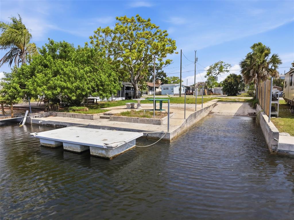 A concrete boat ramp and floating dock sit along a canal near trees and homes — 6737 OSPREY LANE, HUDSON, FL