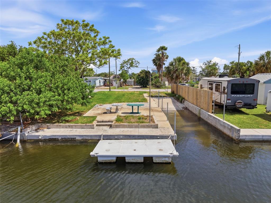 A concrete bulkhead and floating dock sit along a canal next to a grassy lot — 6737 OSPREY LANE, HUDSON, FL