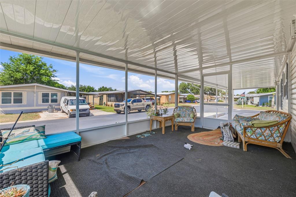 A screened-in porch features a dark carpet, wicker furniture, and views of a residential street — 3125 SHORT LEAF STREET, WESLEY CHAPEL, FL