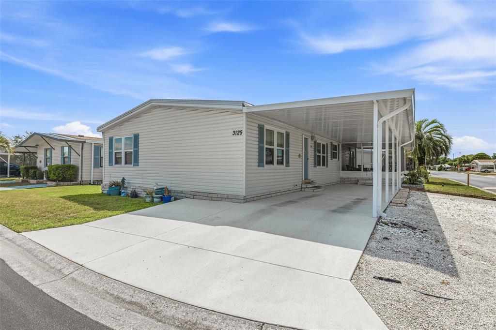 A light-colored mobile home features a concrete driveway, a carport, and blue window shutters — 3125 SHORT LEAF STREET, WESLEY CHAPEL, FL