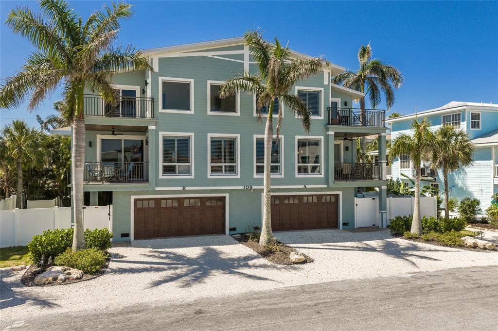 A three-story teal duplex with two garage doors and palm trees in the front yard — 109 6TH STREET N UNIT A & B, BRADENTON BEACH, FL
