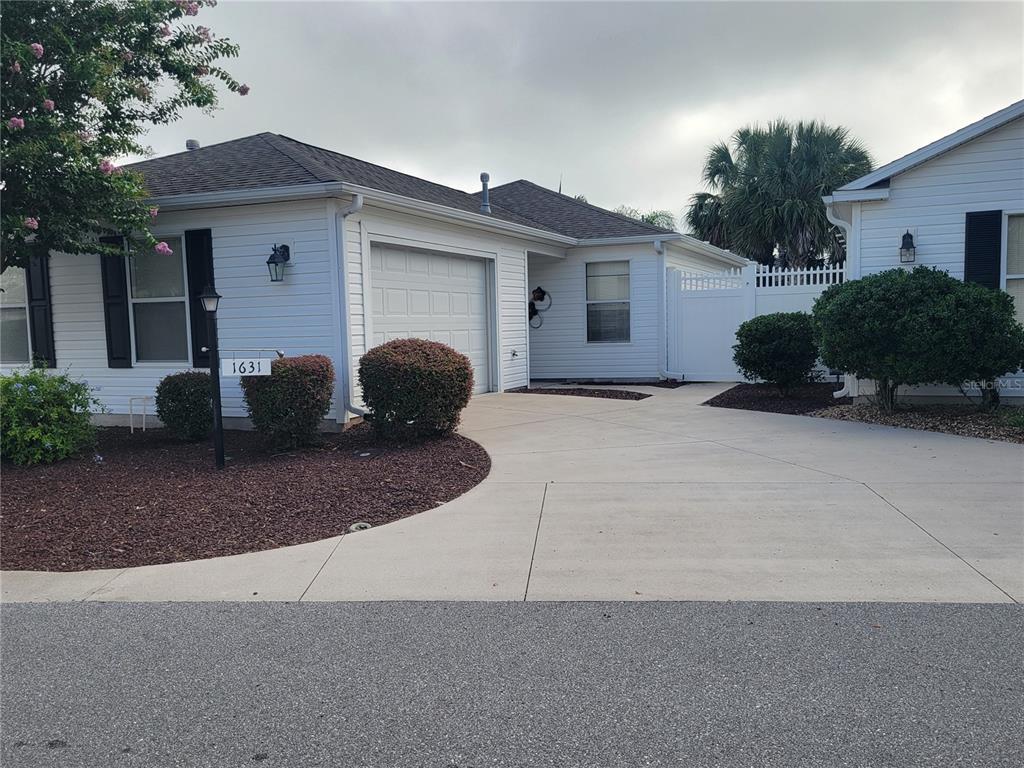 A white single-story house with a garage, driveway, and landscaping under a cloudy sky — 1631 EDISTO LANE, THE VILLAGES, FL