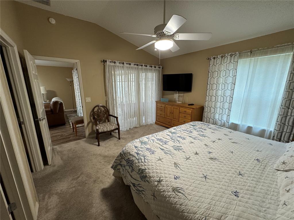 A bedroom features a bed with a coastal quilt, a ceiling fan, and sliding glass doors — 1631 EDISTO LANE, THE VILLAGES, FL