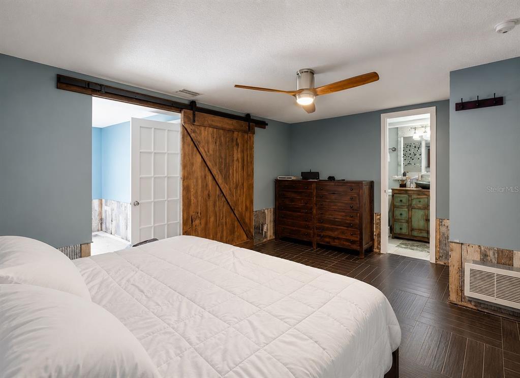 A bedroom features a white bed, a wooden barn door, and a doorway to a bathroom — 5016 MARLIN DRIVE, NEW PORT RICHEY, FL