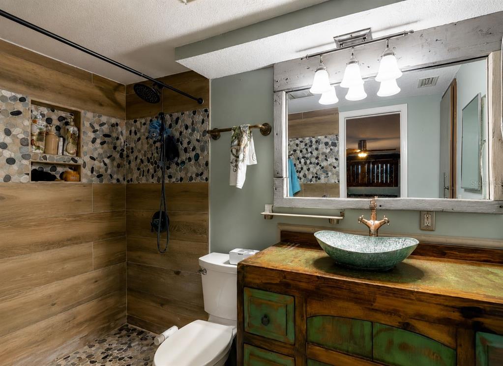 A bathroom features a wood-look tiled shower, a rustic vanity, and a vessel sink — 5016 MARLIN DRIVE, NEW PORT RICHEY, FL