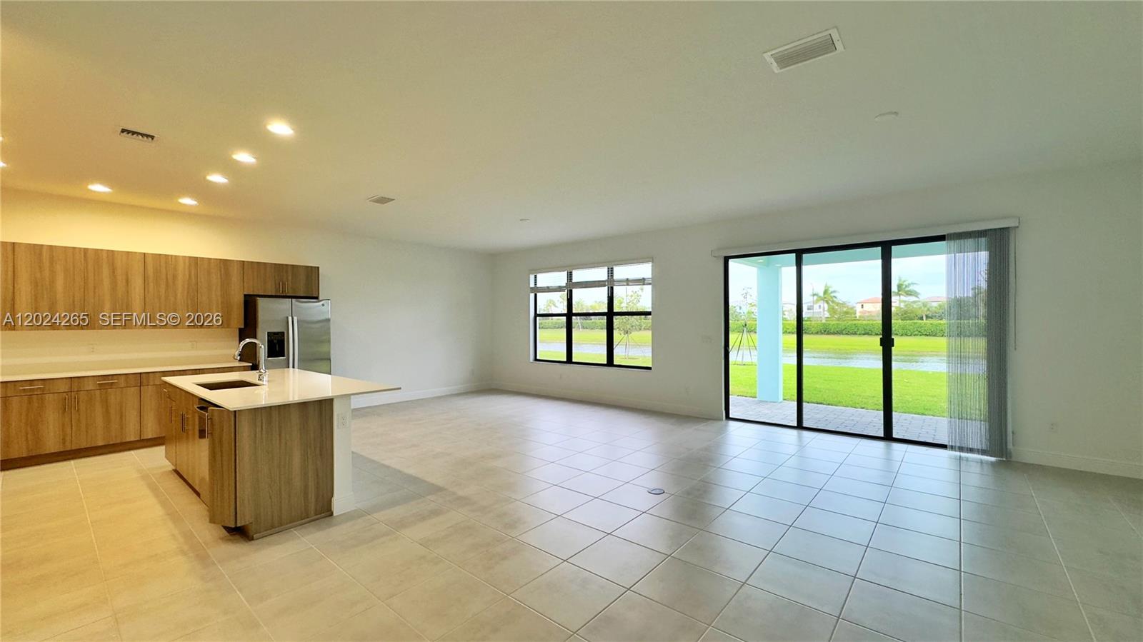 A modern kitchen with wood-look cabinets and an island opens to a spacious tiled living area — 5021 Coquina Pl # 5021, Westlake FL 33470, WESTLAKE, FL
