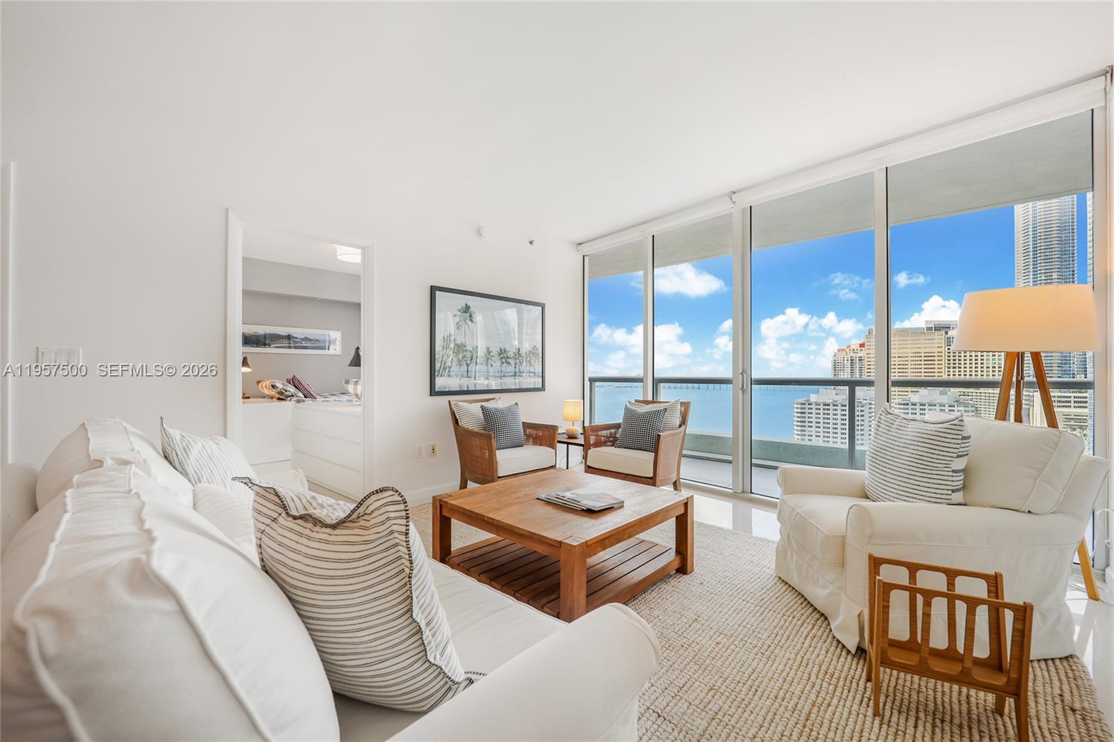 A bright living room features white furniture, a wooden coffee table, and floor-to-ceiling windows — 495 Brickell Ave # 2303, Miami FL 33131, MIAMI, FL