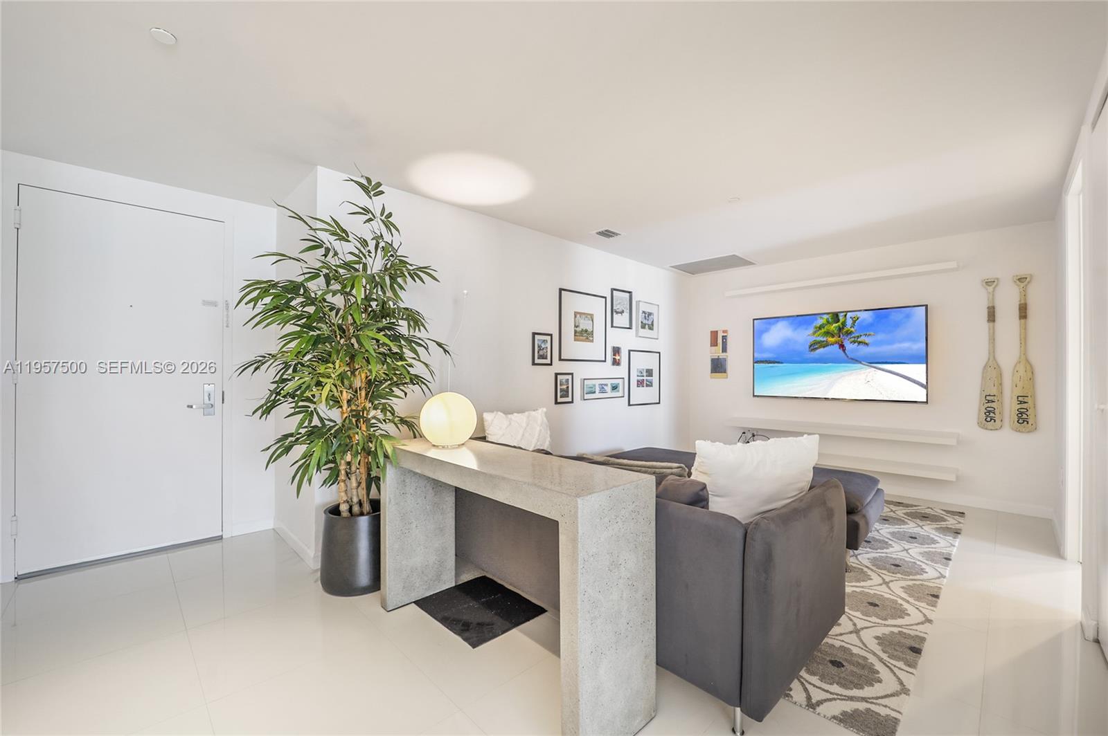 A living room features a grey sofa, a concrete console table, and a wall-mounted television — 495 Brickell Ave # 2303, Miami FL 33131, MIAMI, FL