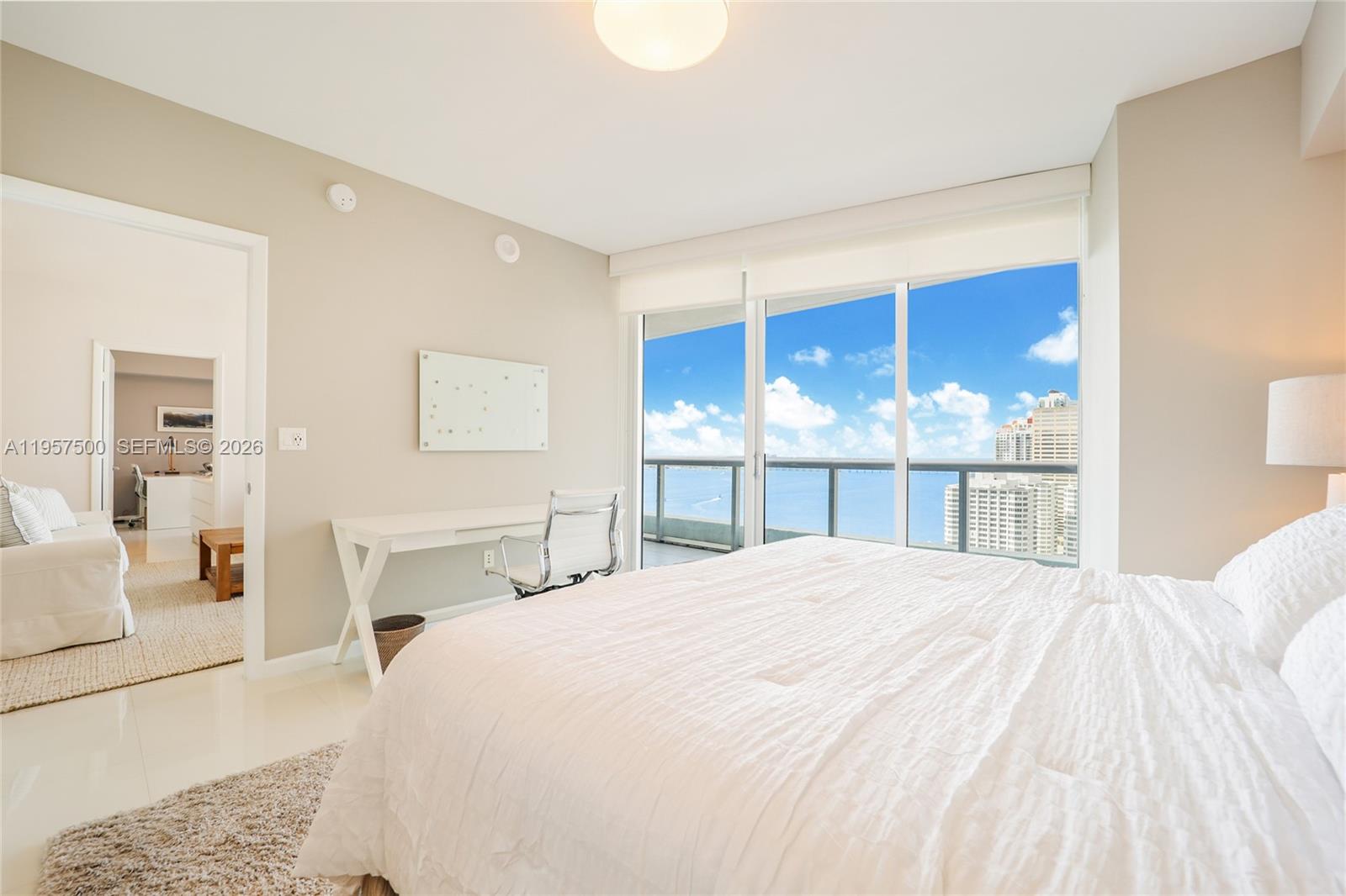 A bedroom with a white bed, desk, and floor-to-ceiling windows overlooking the ocean — 495 Brickell Ave # 2303, Miami FL 33131, MIAMI, FL