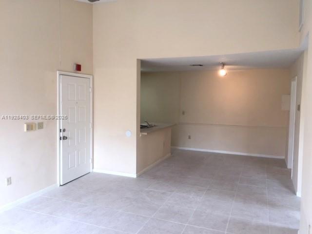 An interior view of a room with light-colored tile flooring and a white entry door — 18324 NW 68 # H, Hialeah FL 33015, HIALEAH, FL