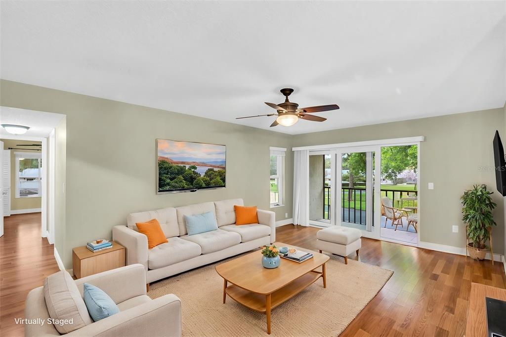 A living room with light green walls, hardwood floors, a ceiling fan, and sliding glass doors — 1400 PINE GLEN LANE UNIT D2, TARPON SPRINGS, FL