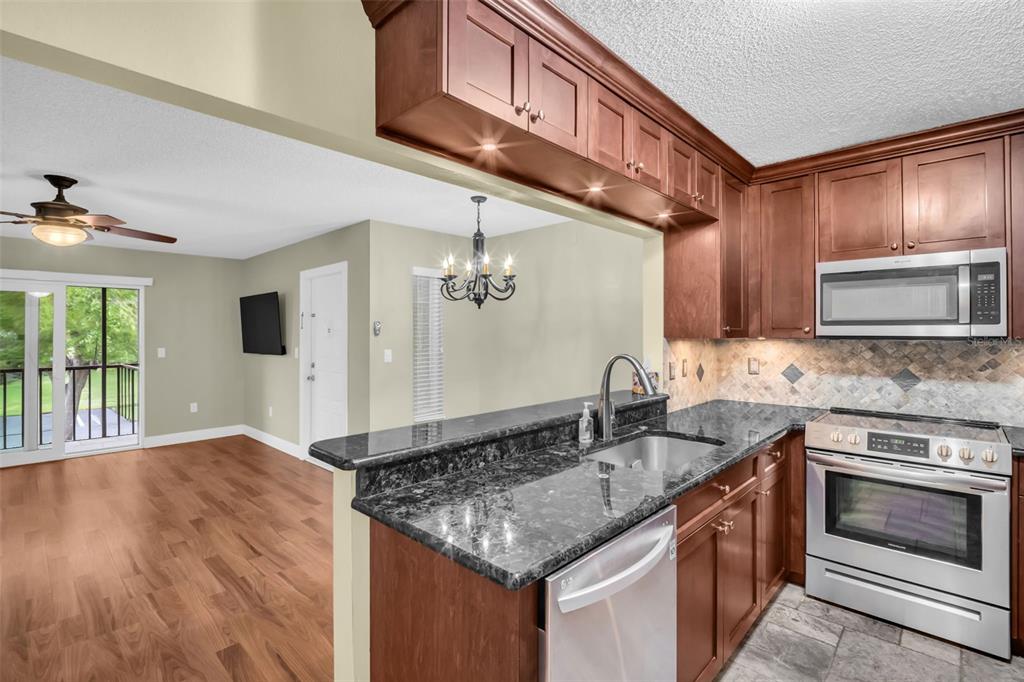 A kitchen with dark wood cabinets and granite countertops overlooks an adjacent living area — 1400 PINE GLEN LANE UNIT D2, TARPON SPRINGS, FL