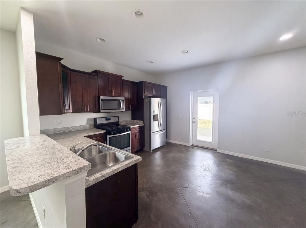 A kitchen features dark wood cabinets, stainless steel appliances, granite countertops, and concrete flooring — 2953 WHISPERING TRAILS DRIVE, WINTER HAVEN, FL