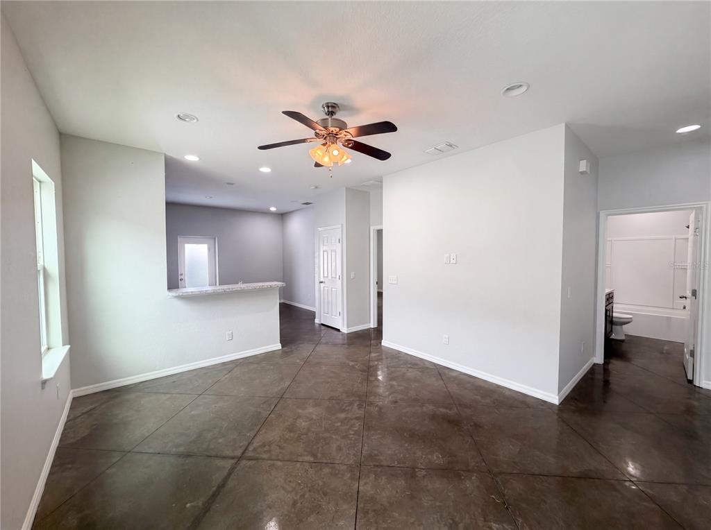 An open-concept living area features dark stained concrete floors, a ceiling fan, and a breakfast bar — 2953 WHISPERING TRAILS DRIVE, WINTER HAVEN, FL