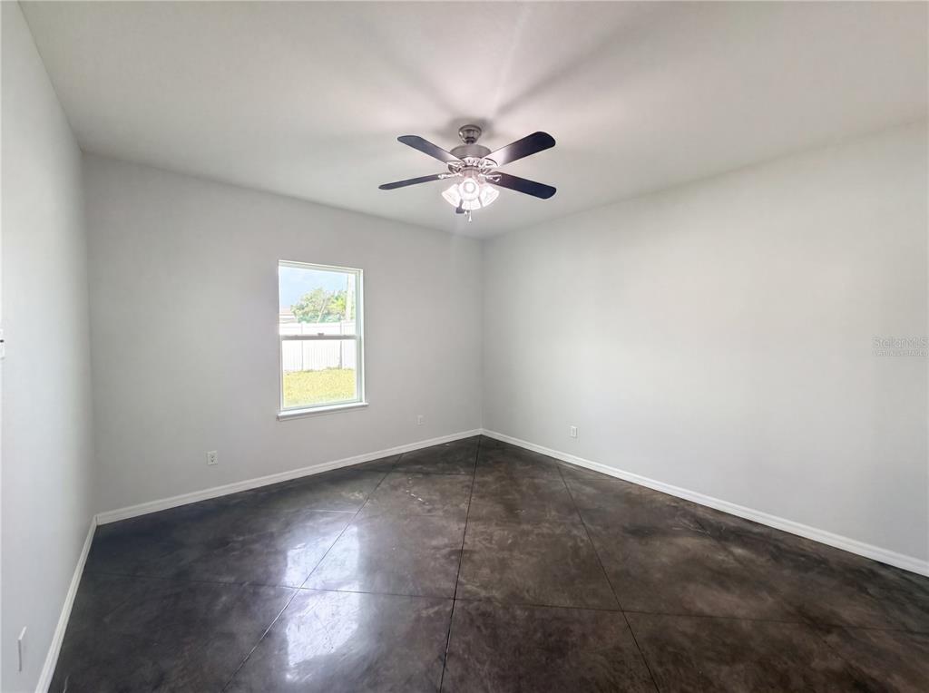 An empty bedroom features light gray walls, a ceiling fan, and dark stained concrete flooring — 2953 WHISPERING TRAILS DRIVE, WINTER HAVEN, FL