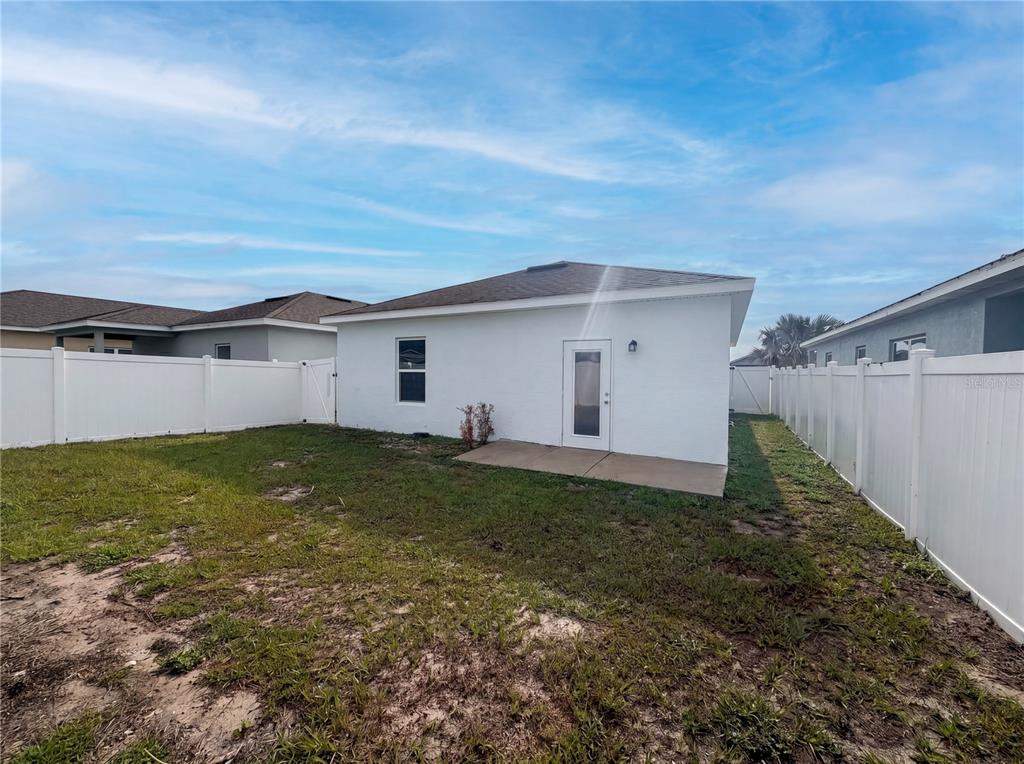 The backyard features a white stucco house with a concrete patio and vinyl fencing — 2953 WHISPERING TRAILS DRIVE, WINTER HAVEN, FL