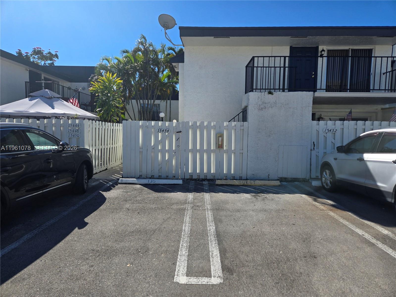 A white fence separates two parking spaces in front of a two-story residential building — 15454 SW 85th Ln # 135, Miami FL 33193, MIAMI, FL