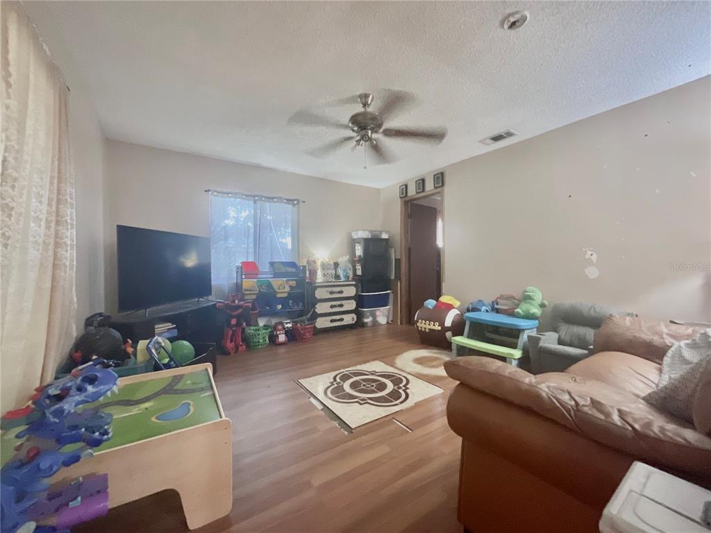 A living room with wood-look flooring, a ceiling fan, a television, and various children's toys — 136 PUELBA LANE, KISSIMMEE, FL