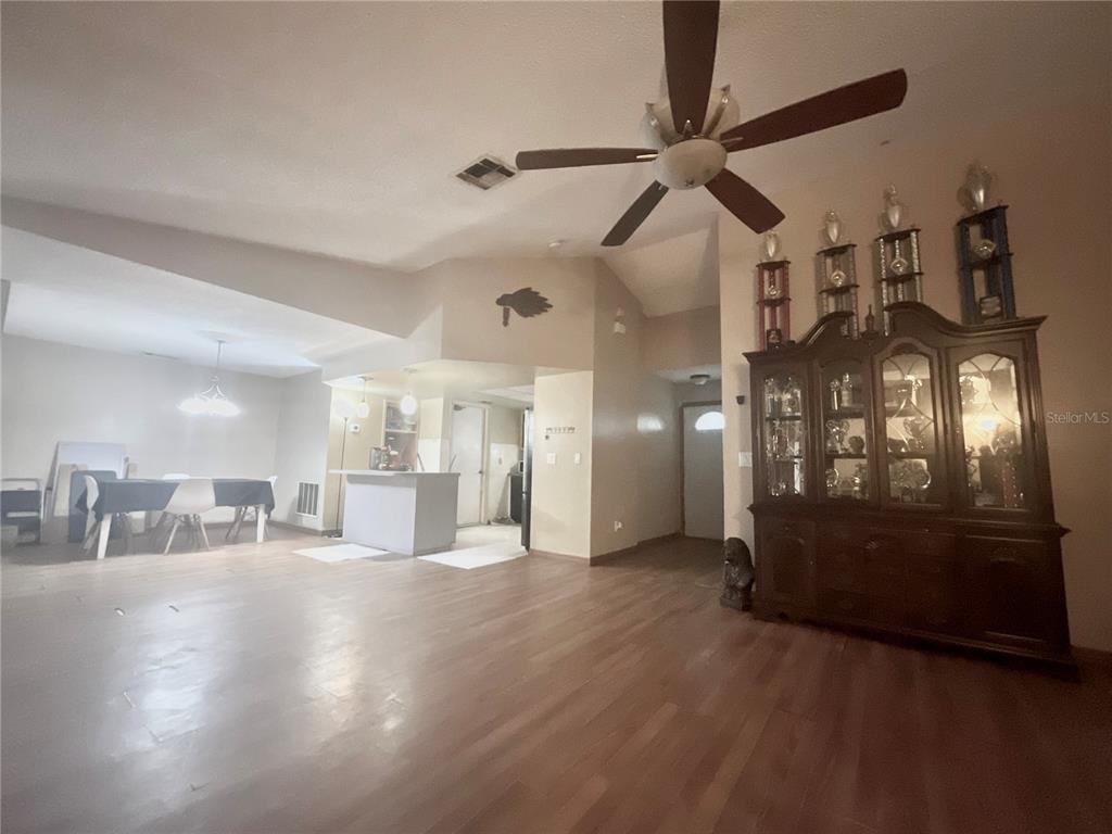A living room with wood-look flooring, a ceiling fan, and a large dark wood china cabinet — 136 PUELBA LANE, KISSIMMEE, FL