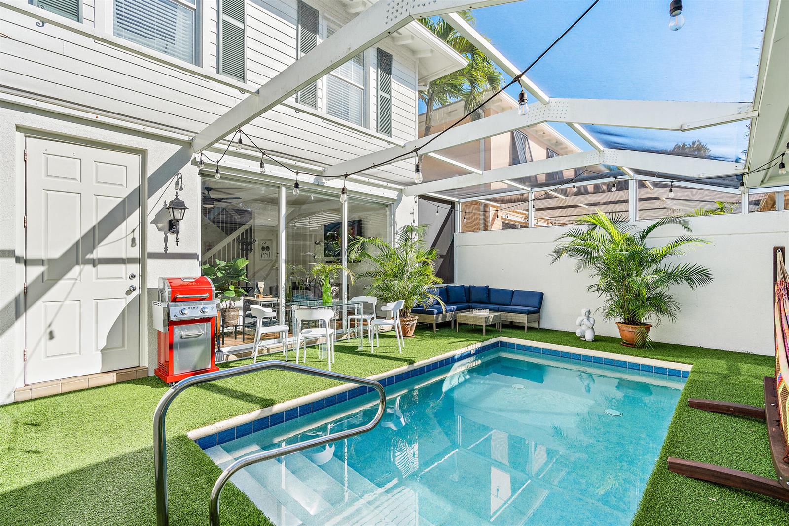 A backyard patio features a small swimming pool, artificial turf, a grill, and lounge seating — 116 Caravelle Drive, Jupiter FL 33458, JUPITER, FL