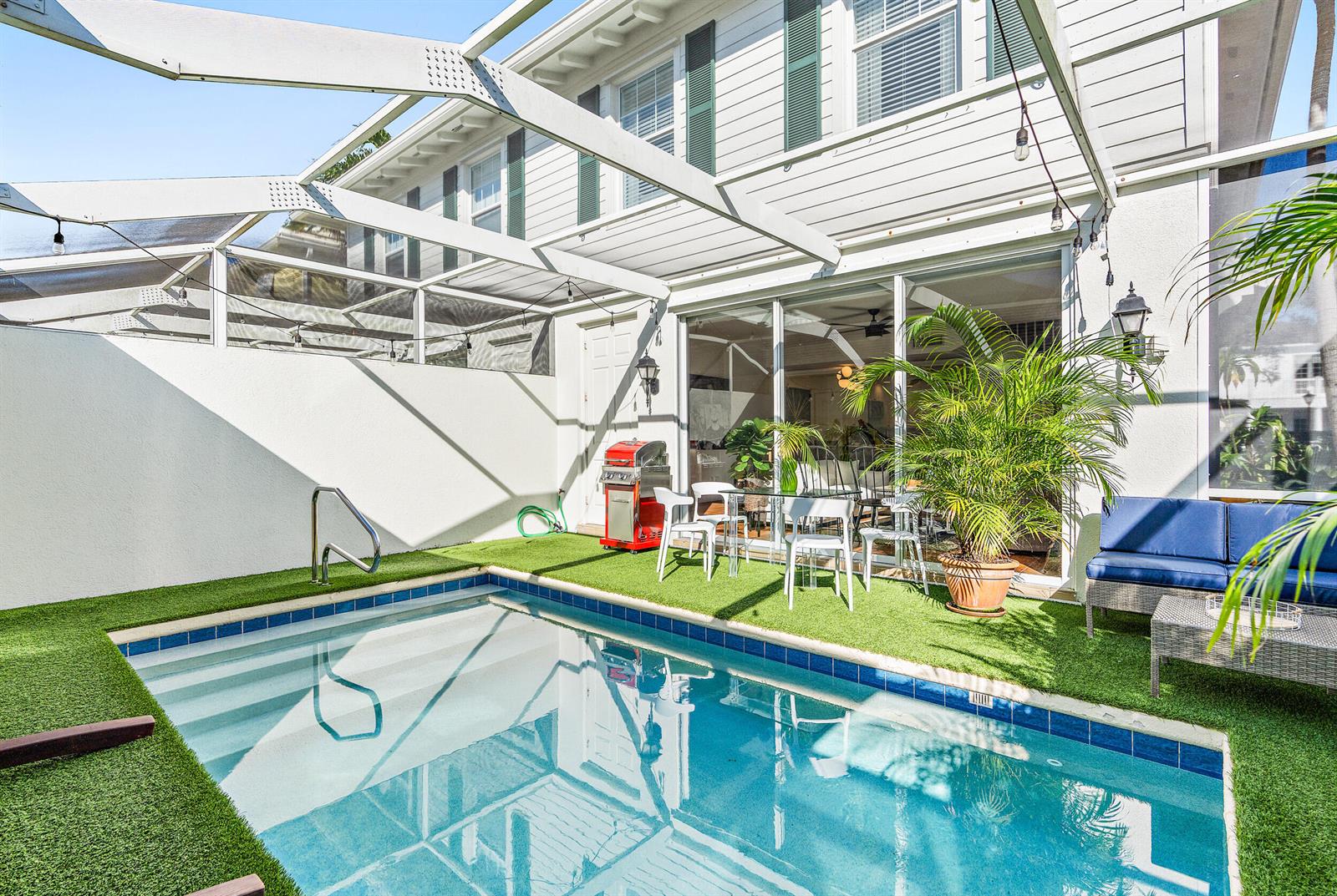 A small backyard pool with artificial turf sits beneath a screened-in patio enclosure — 116 Caravelle Drive, Jupiter FL 33458, JUPITER, FL