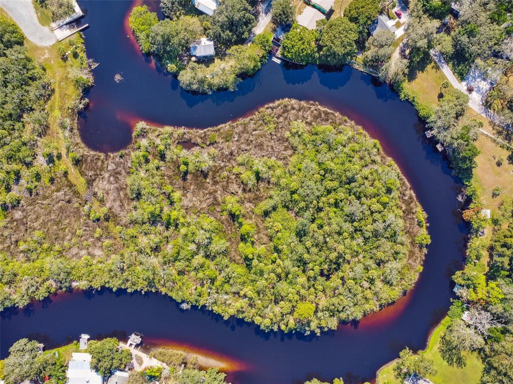 An aerial view shows a winding river surrounding a dense, tree-covered island — 0 JAPONICA COURT, NEW PORT RICHEY, FL