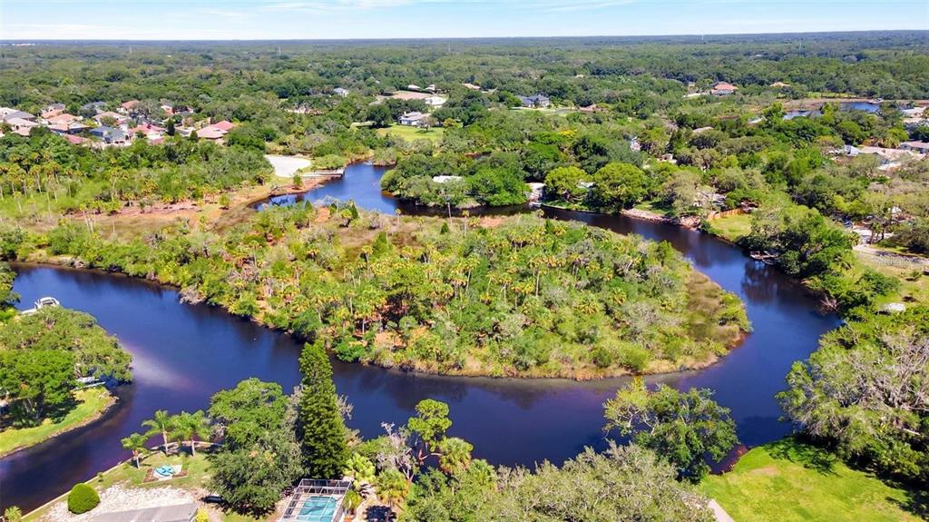 An aerial view shows a winding river surrounded by dense trees and residential homes — 0 JAPONICA COURT, NEW PORT RICHEY, FL