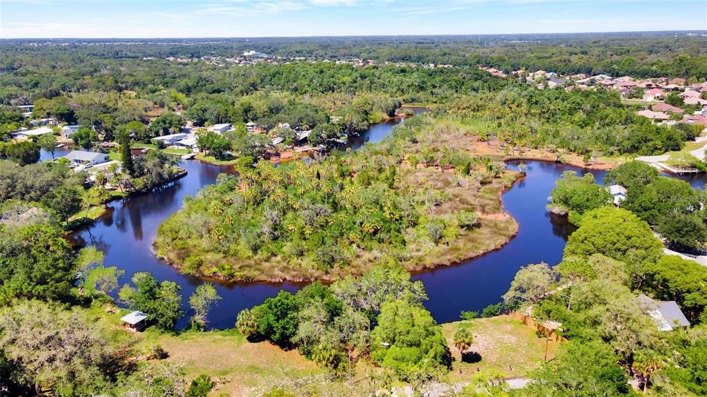 An aerial view shows a winding river surrounded by dense trees and residential properties — 0 JAPONICA COURT, NEW PORT RICHEY, FL