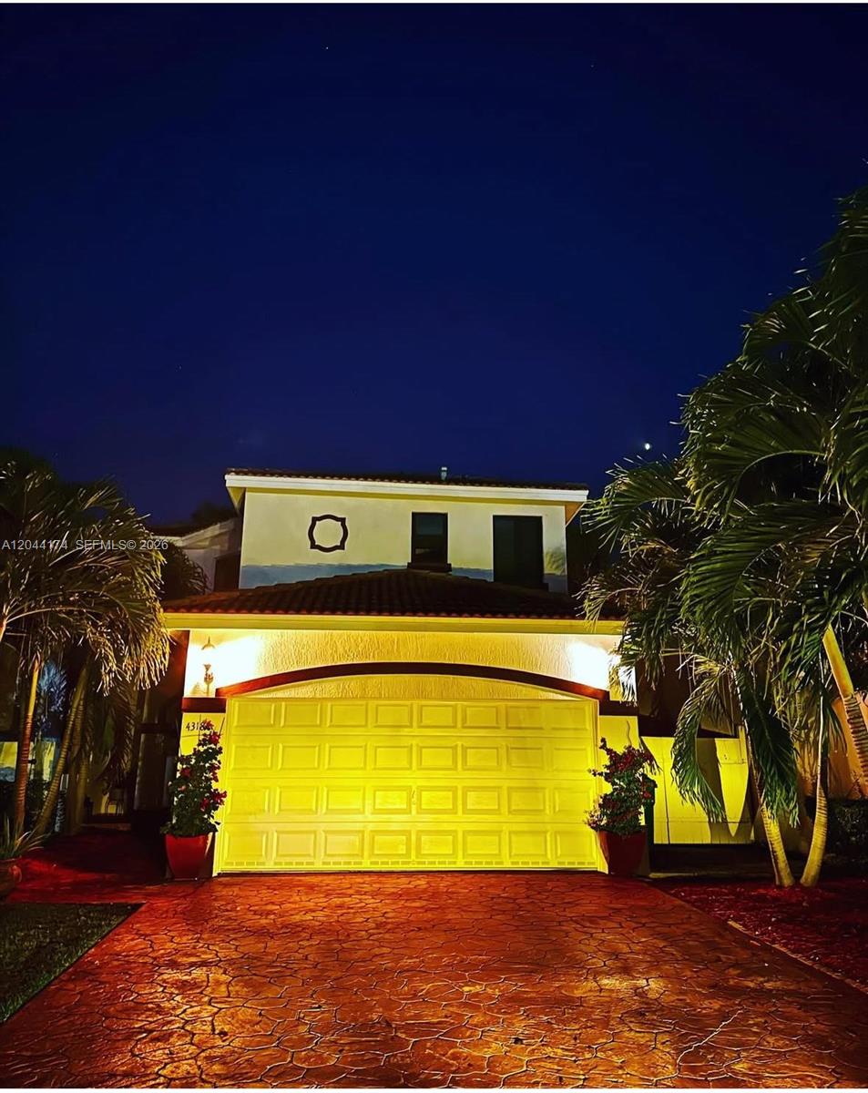A two-story house with a yellow garage door and a red stamped concrete driveway at night — 4318 NW 113th Pl, Doral FL 33178, DORAL, FL