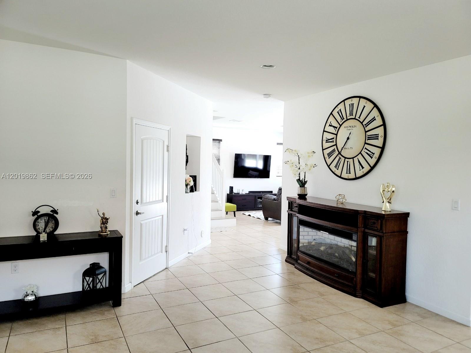 A bright entryway features tile flooring, a large wall clock, and a fireplace console — HOMESTEAD, FL