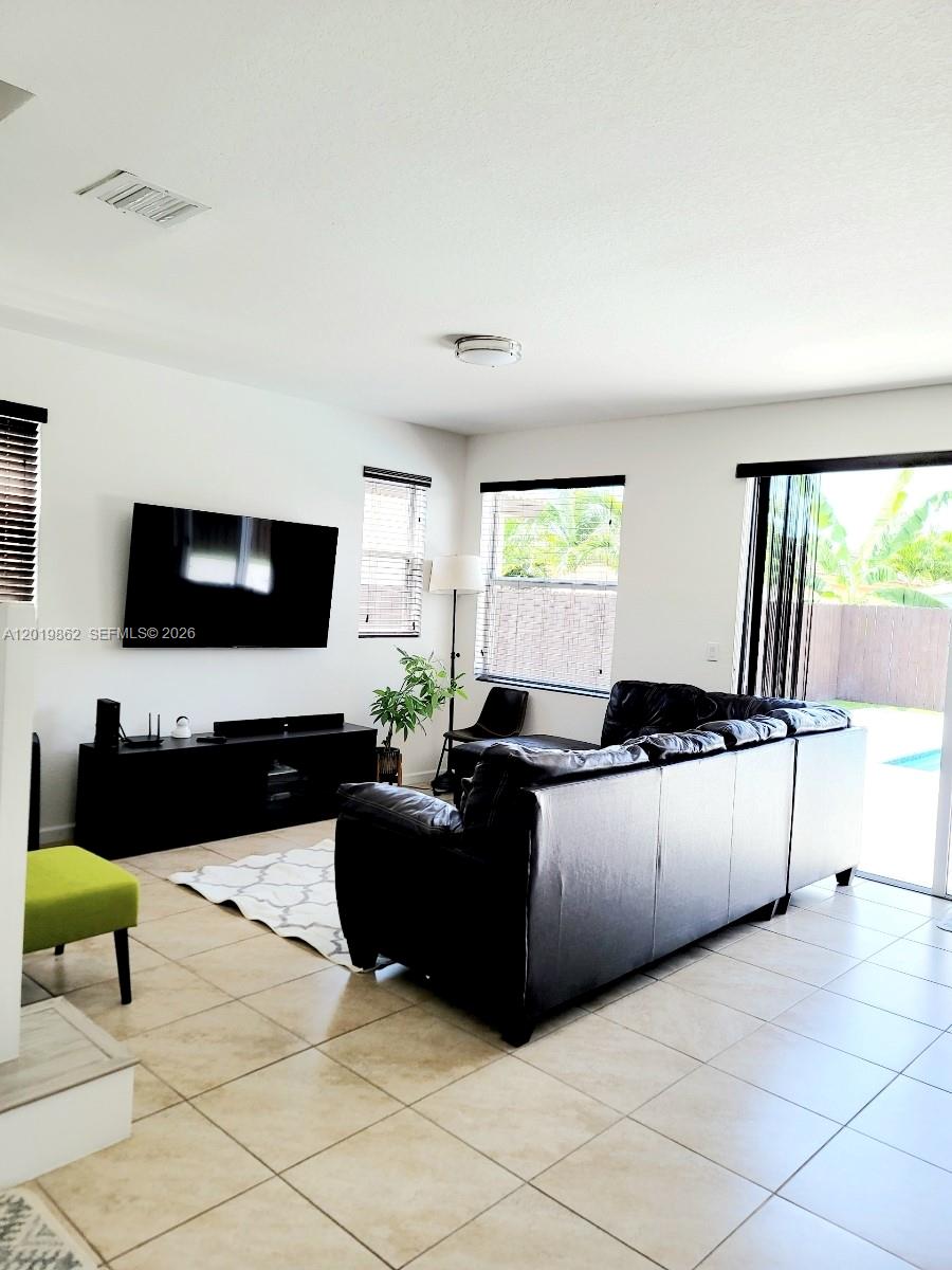 A living room features a black leather sectional, a wall-mounted television, and tile flooring — HOMESTEAD, FL