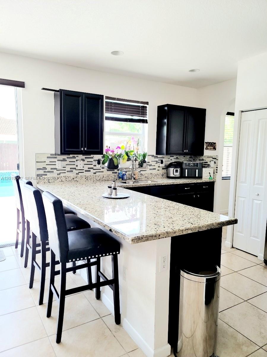 A kitchen features black cabinets, a granite countertop island with bar stools, and tiled floors — HOMESTEAD, FL