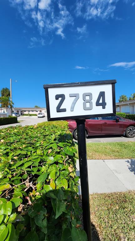A black metal sign displays the house number 2784 in front of a green hedge — 2784 DUDLEY DRIVE E UNIT E, WEST PALM BEACH, FL