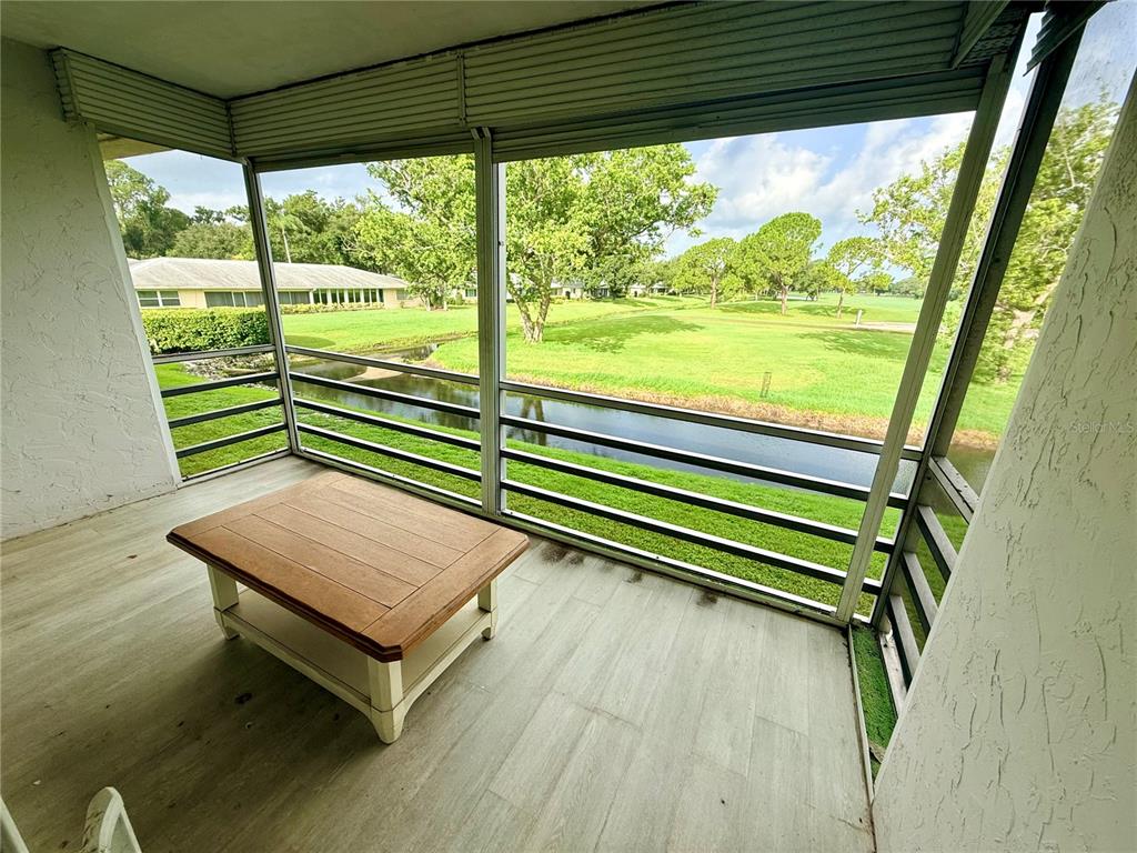 A screened-in balcony with light wood-look flooring overlooks a small canal and a golf course — 7880 PALM AIRE LANE UNIT 203, SARASOTA, FL