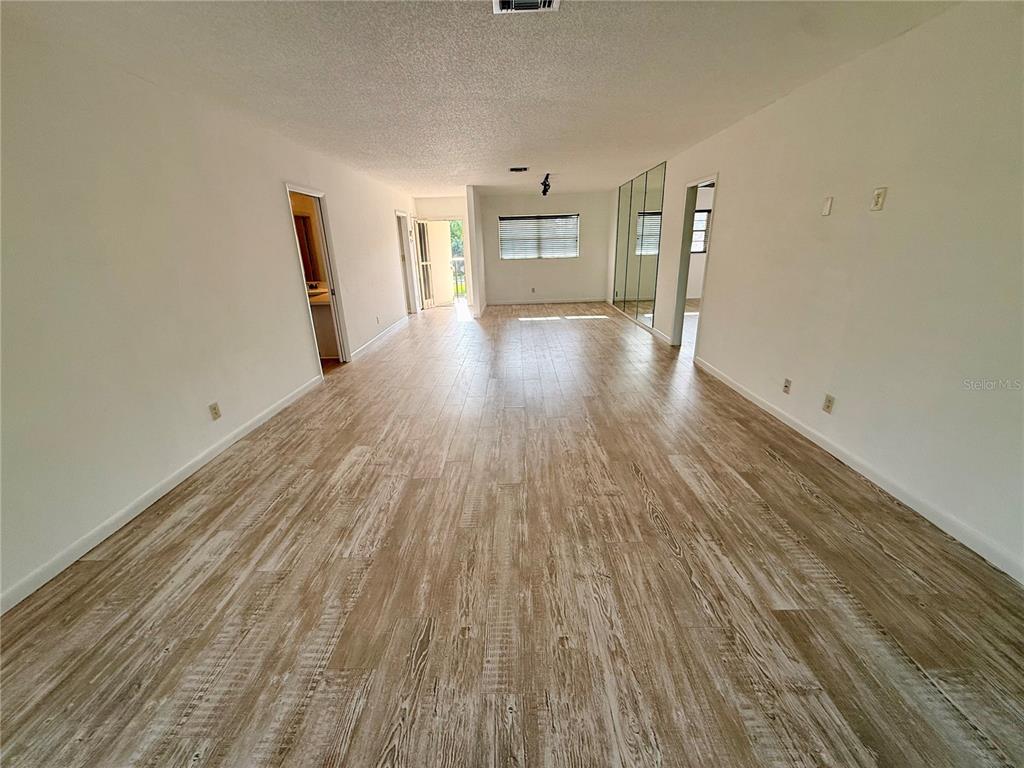 An empty room with light wood-look flooring, white walls, and a mirrored closet wall — 7880 PALM AIRE LANE UNIT 203, SARASOTA, FL