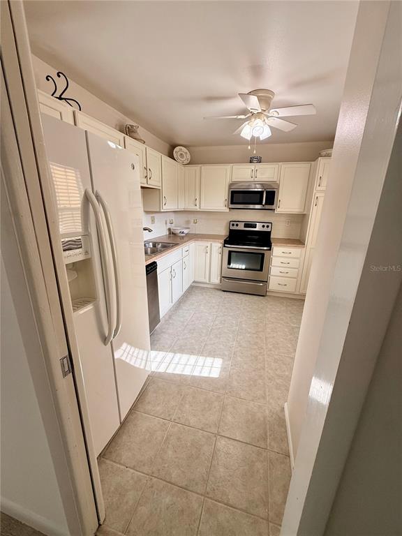 A kitchen features white cabinets, stainless steel appliances, and light-colored tile flooring — 7880 PALM AIRE LANE UNIT 203, SARASOTA, FL