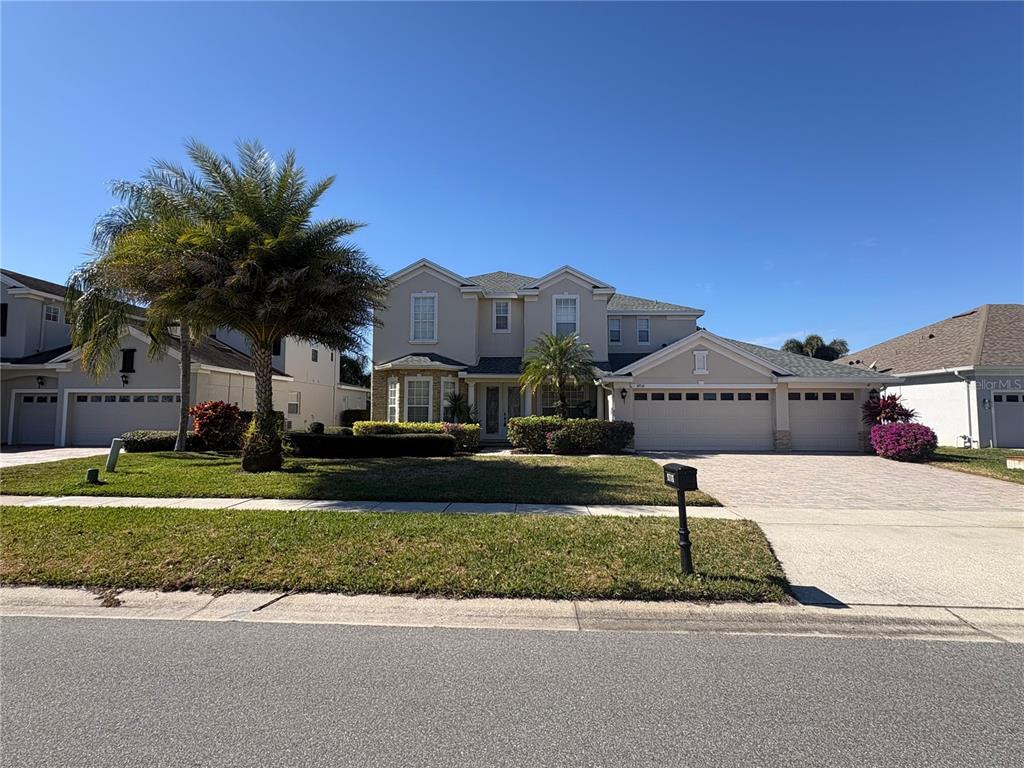 A two-story suburban house with a three-car garage, palm trees, and a paved driveway — 9718 PINEOLA DRIVE, ORLANDO, FL