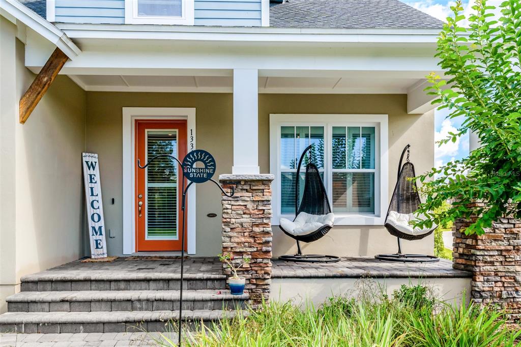 A front porch features a bright orange door, two hanging chairs, and stone pillar accents — 13347 GABOR AVENUE, ORLANDO, FL