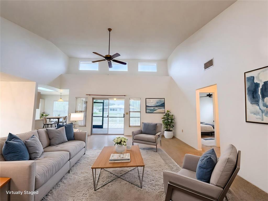 A living room with vaulted ceilings, a ceiling fan, and sliding glass doors to a patio — 712 45TH STREET E, BRADENTON, FL