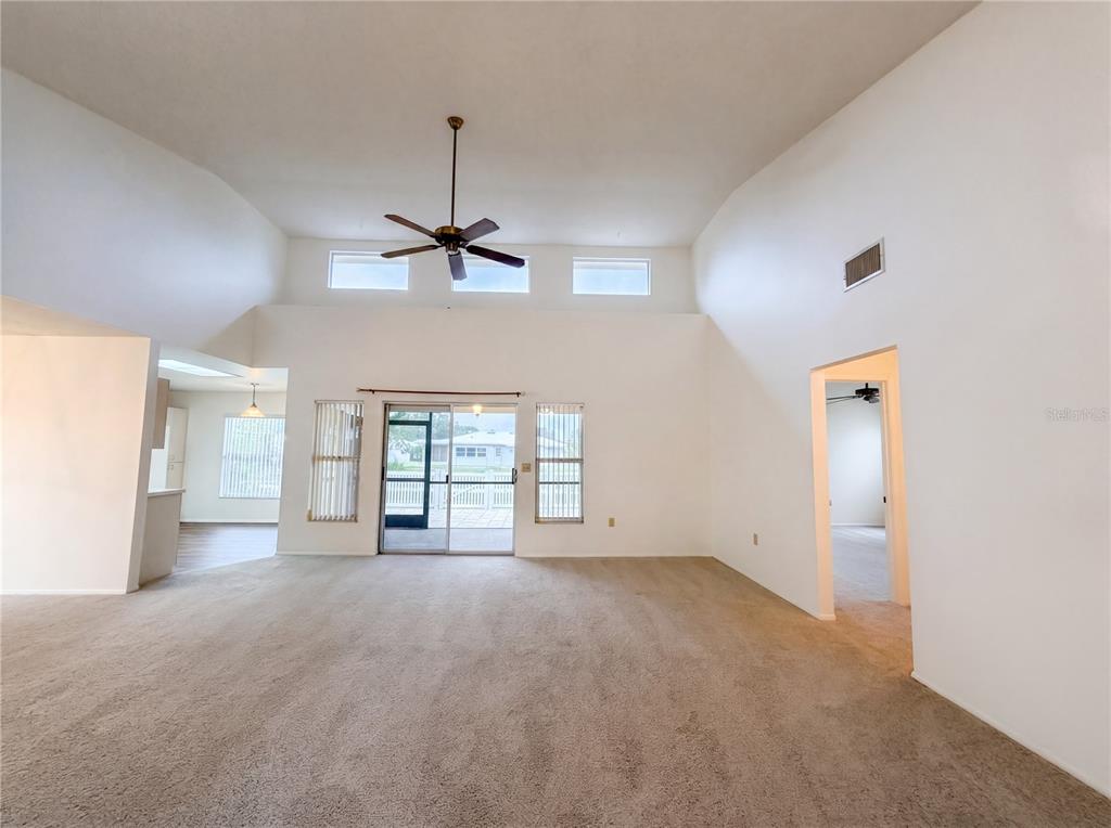 A spacious living room with high ceilings, carpeted floors, and a sliding glass door — 712 45TH STREET E, BRADENTON, FL