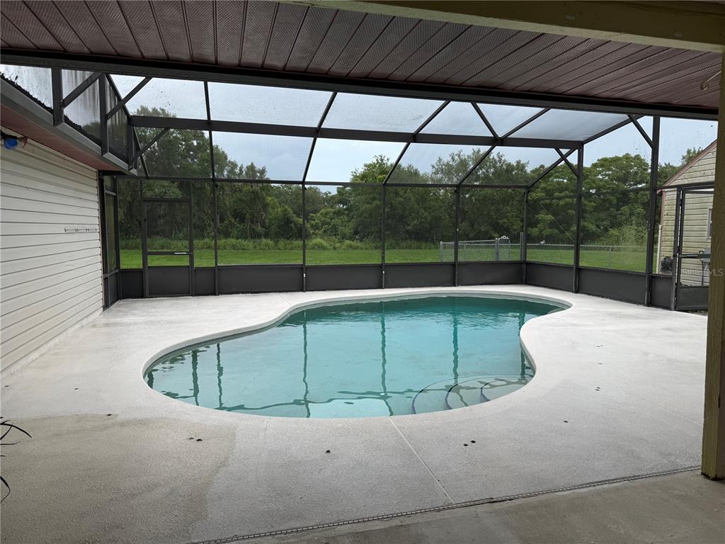 A kidney-shaped swimming pool sits on a concrete patio enclosed by a screened-in lanai — 4125 E VISTA COURT, KISSIMMEE, FL