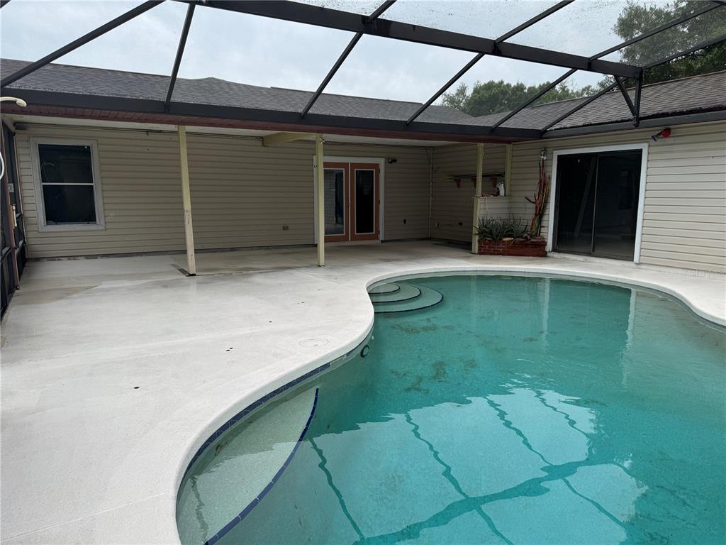 A screened-in patio features a curved swimming pool with steps and beige siding — 4125 E VISTA COURT, KISSIMMEE, FL