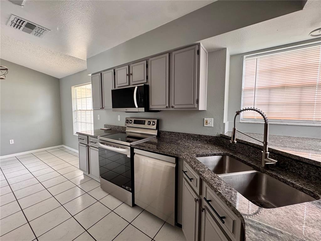 A kitchen features gray cabinets, granite countertops, stainless steel appliances, and white tile flooring — 4125 E VISTA COURT, KISSIMMEE, FL