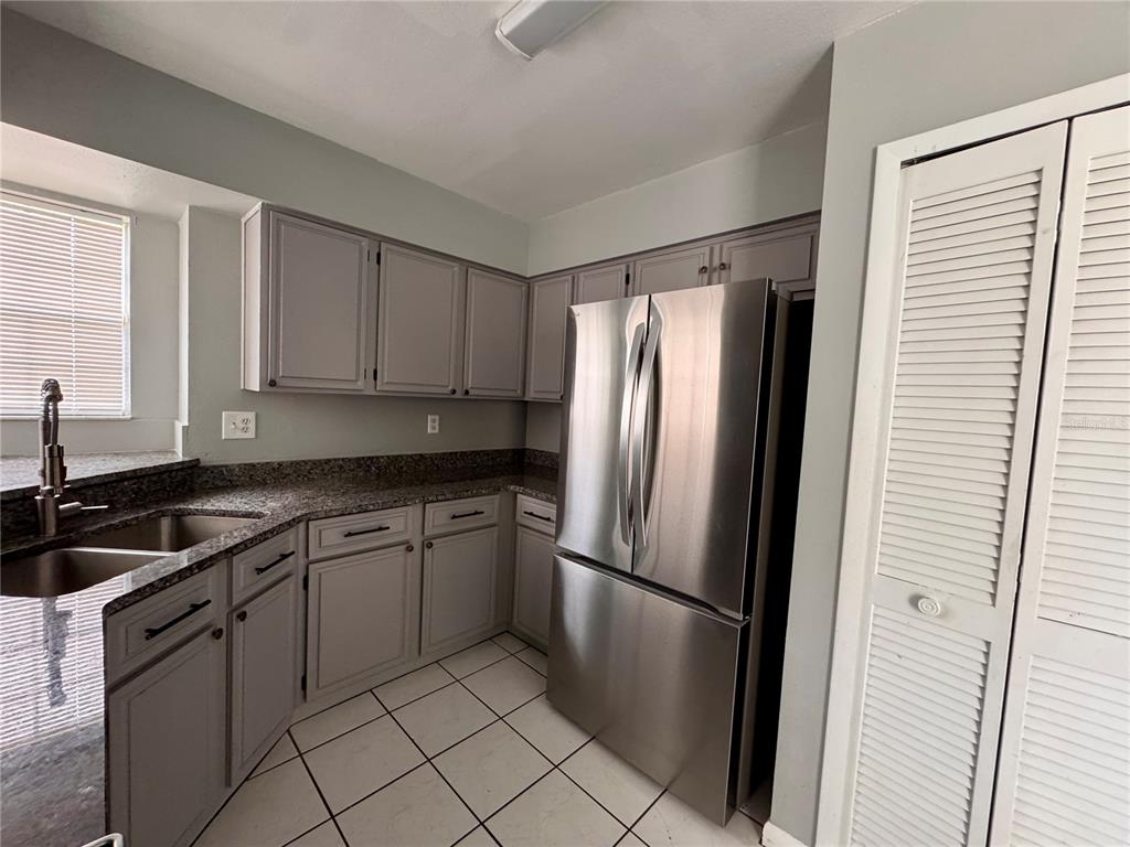 A kitchen features gray cabinets, granite countertops, stainless steel appliances, and white tiled flooring — 4125 E VISTA COURT, KISSIMMEE, FL