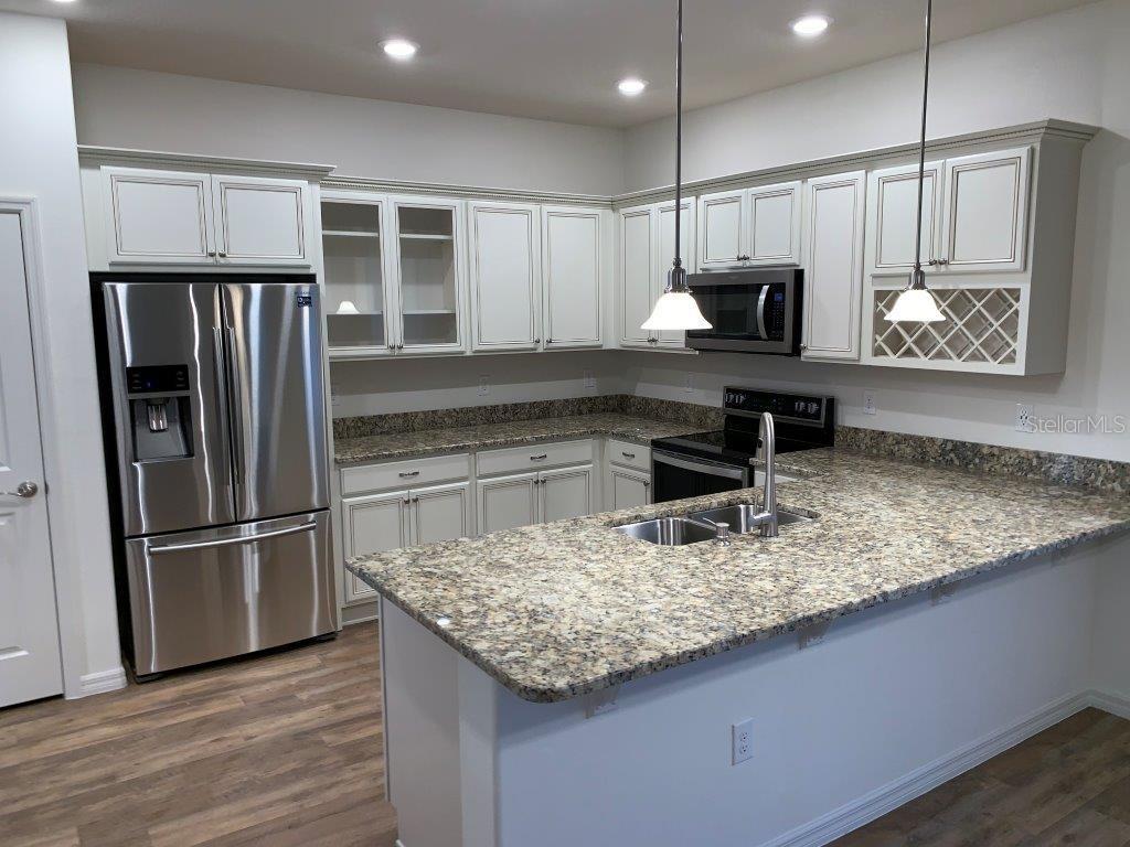 A kitchen features white cabinetry, granite countertops, stainless steel appliances, and a central island — 3013 CHERRY ORCHARD LANE, WINTER GARDEN, FL